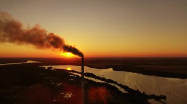Akşamları nehir kıyısındaki fabrikada. Günbatımında doğadaki endüstriyel borulardan siyah duman çıkıyor. Çevredeki hava kirliliği.