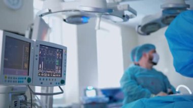 Yoğun bakım ünitesindeki sağlık monitörleri. Cerrahi işlemin arka planında hastanın hayati belirtilerini gösteren ekranlar. Sağlık hizmeti kavramı.