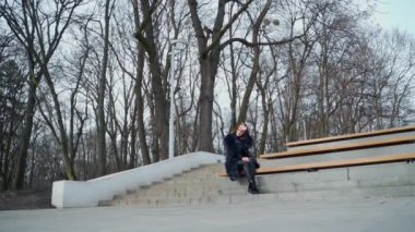 Kız parkta bankta oturuyor. Yapraksız ağaçların arka planında pofuduk ceketli güzel bir kadın tek başına oturuyor. Aşağıdan görüntüle.