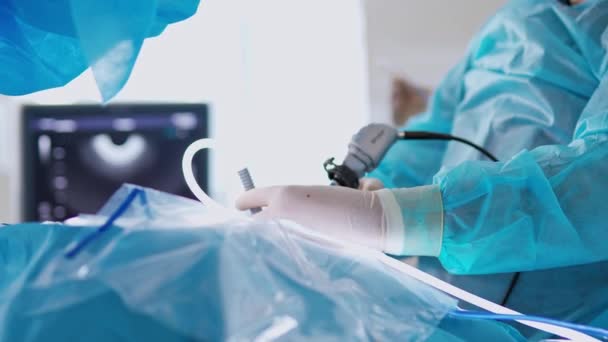 医師の手の中にある手術器具 モニターの背景に最新の機器を搭載した手術を行う滅菌手袋の医療専門家 クローズアップ — ストック動画