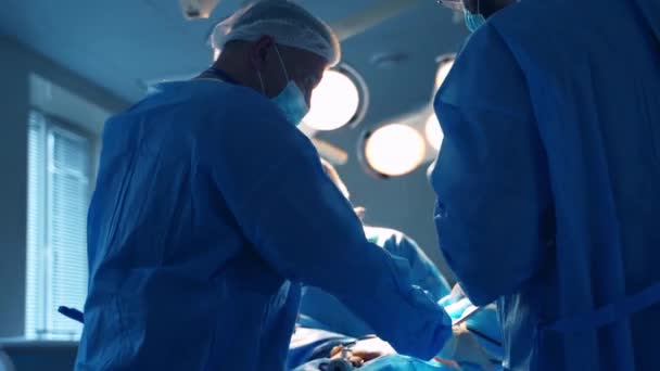 Grupa Chirurgów Lekarze Niebieskim Mundurze Wykonują Zabieg Pacjencie Przeciwko Lampie — Wideo stockowe