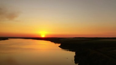 Turuncu gün batımı. Güneşin batışının renkli gökyüzünün altındaki nehrin güzel manzarası. Su yüzeyinde inanılmaz bir gün batımı. Hava görünümü.