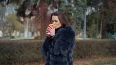 Güzel kız dışarıda kahve içer. Tüylü, sıcak içecekle kameraya bakan şık bir kadının portresi. Parkta şık bir model.