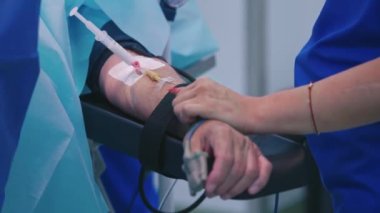 Klinikte şırıngalı bir hasta kolu. Tıbbi hemşire ameliyat sırasında borularla hastanın elinin yanında duruyor. Yakın plan. Sağlık hizmetleri kavramı.