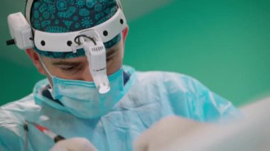Kafasında mikroskop olan genç bir doktor. Cerrahın yüzünü ameliyat ederken uzman doktorların elleri. Yakın plan..