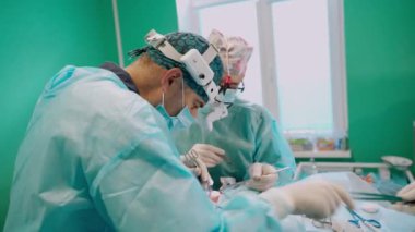 Ameliyathanede cerrahi işlem. Tıp üniformalı doktorlar cerrahi aletlerle ameliyat yapıyorlar. Hemşire cerrahlara steril aletler veriyor..