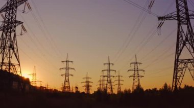 Yüksek voltajlı kulelerin silueti. Enerji istasyonundaki elektrik direkleri gün batımında güzel gökyüzünün arka planında. Elektrik santrali ve yüksek voltajlı elektrik hatları. Aşağıdan görüntüle.