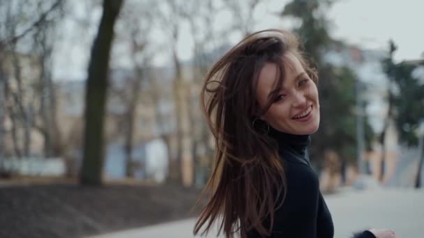 公園でハッピーな女の子が回ってくる 黒いセーターの長い髪の魅力的な若い女性は カメラを見て 街の通りで微笑んでいる スローモーション — ストック動画