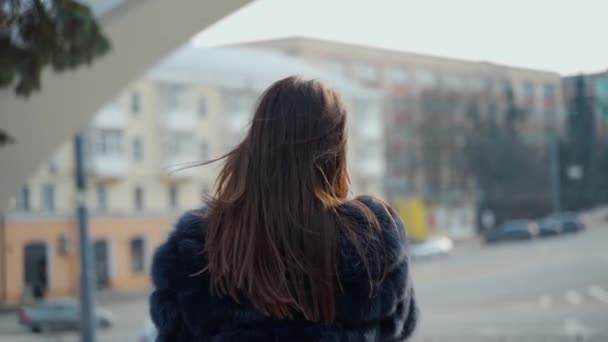 屋外で電話するスタイリッシュな女の子 毛皮のコートを歩いている若いブルネットの女性は 街の背景で携帯電話を話します スローモーション — ストック動画