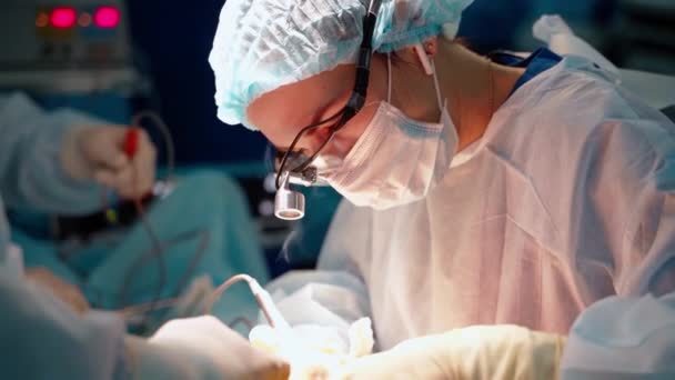 医師は医療機器を使用しています 患者の手術を行う頭の上にグラスを拡大する女性スペシャリスト — ストック動画