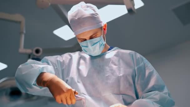 男性医師が制服を着ている 手術室に無菌医療ツールを搭載したマスク手術患者の外科医の肖像画 下からの眺め — ストック動画