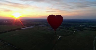 Kırmızı Aerostat batan güneşe karşı. Sıcak hava balonu kırsal alanda gökyüzünde uçuyor. Kalp şeklinde sıcak hava balonu. Hava görünümü.