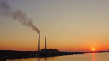 Turuncu gökyüzüne karşı dumanlı bitki. Gün batımında doğa arasındaki endüstri. Havadaki fabrikadan yayılan zararlı duman.