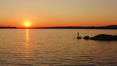 İnsanlar gün batımında balık tutuyor. Akşam gökyüzünde güzel turuncu güneş. Elinde olta olan siluet balıkçıları taşın üstünde balık tutuyor. Erkekler suyun yanında rahatlar..