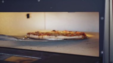 Pizza fırında hazırlanıyor. Şef fırının kapısını açıyor ve pizzanın hazır olup olmadığını kontrol ediyor. Aşçı pizzanın hazır olup olmadığını pizza halkasıyla kontrol eder..