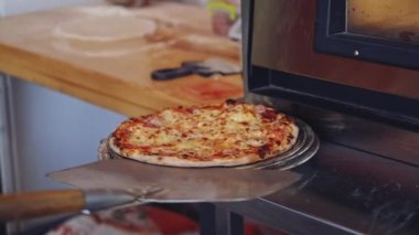 Pizza hazır. Pizzacı pizza yapıyor. Pizza spatulasını kullanarak pizzayı fırından çıkaran şef. Aşçı bitirilmiş pizzayı tabağa koyar. Lezzetli pizza.