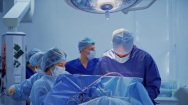 Bir grup tıbbi uzman ameliyathanede. Mavi üniformalı doktorlar tıbbi lambanın altında ameliyat yapıyorlar. Sağlık hizmeti kavramı.