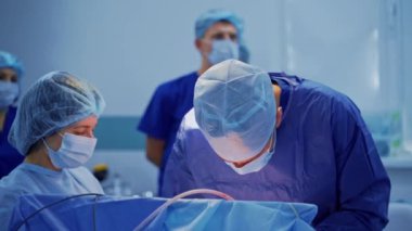 Ameliyathanede ameliyat. Mavi üniformalı doktorlar bir operasyon düzenliyor. Bir grup genç doktor klinikteki cerrahi süreci gözlemliyor.
