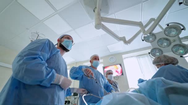 手術中の医師のチームワーク ブルーユニフォームの医療専門家は 手術室で患者を操作する 動作する劇場の現代装置 下からの眺め — ストック動画