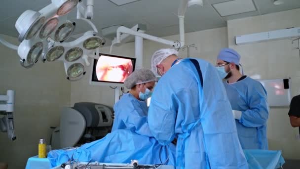 手術室の外科医のチーム モニターのスクリーンは 病院の患者の手術プロセスを示しています 現代の外科室と医師のグループ — ストック動画