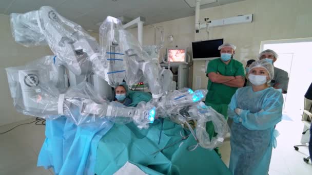 ロボットを含む医療活動 マスクの医師グループは モニター上のロボット手術を観察します フューチャーメディカル — ストック動画