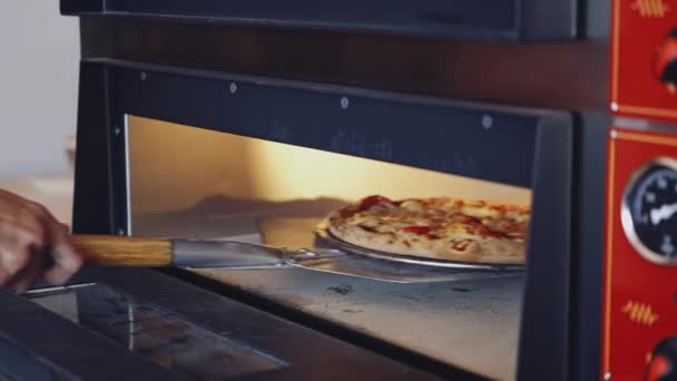 ホットおいしいピザ ピッツェリアマスターはオーブンからピザを取り出します シェフはキッチンで特別なピザスパチュラで新鮮なピザを引き出しています — ストック動画