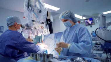 Cerrahlar ameliyat yapar ve mikroskop kullanır. Tıbbi üniformalı doktor ve bayan asistan modern ameliyathanede beyin cerrahisi yapıyor..