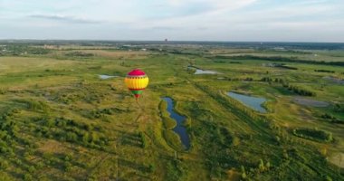 Renkli aerostat. Güzel sıcak hava balonu yeşil tarlaların arka planında ve kırsal alandaki küçük göllerde havada seyahat eder. Hava görünümü.