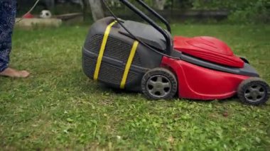 Çim biçme makinesi bahçede çalışıyor. Arka bahçede çim biçme makinesiyle çim biçen bir kadın. Yazın bahçıvanlık..