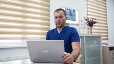 Teletıp. Masasında oturan bir tıp uzmanı ve ofisinde video görüşmesi yapan bir hastaya danışmanlık yapıyor. Uzaktan muayene sırasında dizüstü bilgisayar kullanan erkek terapist.