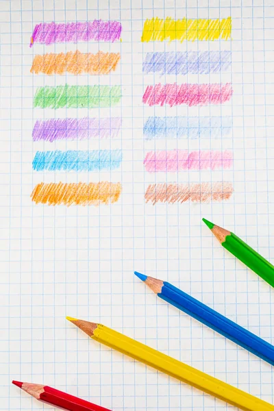 A Rainbow of Colors: Colored Pencils Lined Up on a Sheet of Paper. Colored pencils are lined up on a sheet of paper