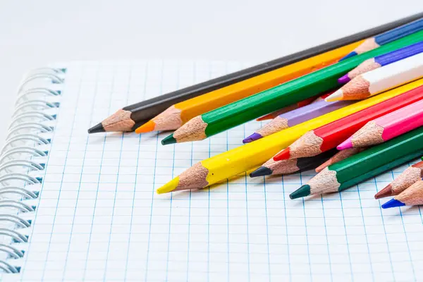 A Rainbow of Creativity: Colored Pencils Resting on a Notebook. A group of colored pencils sitting on top of a notebook