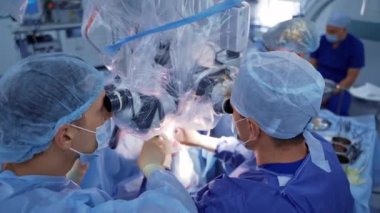 Ameliyathanede doktorların takım çalışması. Cerrahlar hastanedeki bir hastaya ameliyat sırasında mikroskop kullanırlar. Üst görünüm.