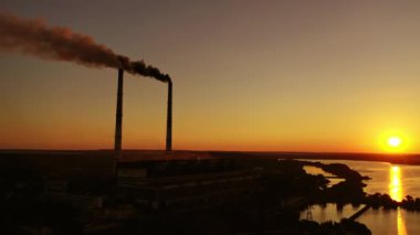 Gün batımında doğa arasında zararlı bir fabrika. Tehlikeli dumanlar endüstriyel boruların havasını dolduruyor. Alacakaranlıkta üretim. Çevre tehlikede. Küresel sıcaklık.