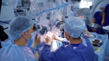 Nörocerrahlar mikroskoba bakarlar. Tıbbi maskeli ve üniformalı profesyonel doktorlar sinir cerrahisi yapar ve modern ekipmanlar kullanır..