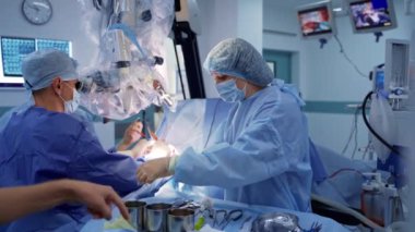 Nöroşirürji prosedürü. Bir grup tıp uzmanı mikroskopa bakarak beyin cerrahisi yapıyor. Hemşire ameliyathanede doktorlara yardım ediyor..