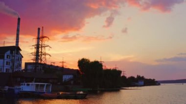 Nehir kıyısında imalat. Endüstriyel bitki ve yüksek voltajlı elektrik kuleleri gün batımında doğa arasında. Nehrin manzarası. Hava görünümü.