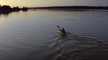 Genç adam gün batımında gölde kayak yapıyor. Alacakaranlıkta gölde bir sandalda yalnız başına yolculuk eden bir adam. Akşamları kürekli bir kayıktaki adam. Hava görünümü.