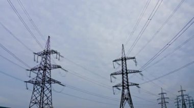 Arka planda yüksek elektrik direkleri. İletişim hatları. Aralarına elektrik kabloları gerilmiş elektrik kuleleri, yüksek voltajlı kablolar. Yavaş çekim.