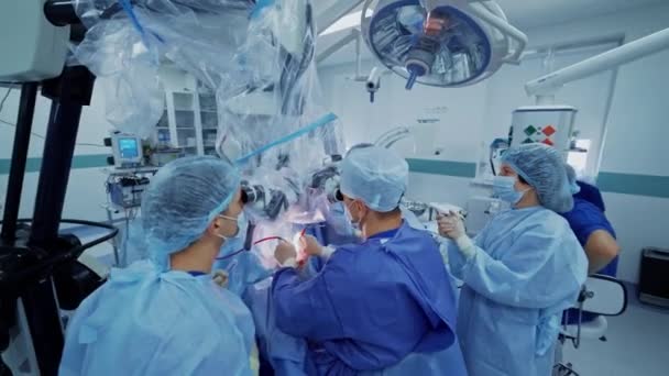 现代外科技术 穿着工作服的一组医生一边检查显微镜一边给病人做手术 — 图库视频影像