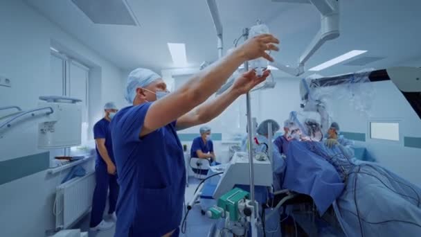男性アシスタントは医療機器を準備しています 医師団が手術を行っている 手術室で働く医療ユニフォームの外科医 — ストック動画