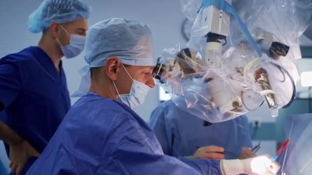 现代神经外科穿着工作服戴口罩的一组医生用显微镜和医疗工具进行神经外科手术 — 图库视频影像