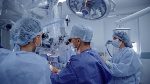 带显微镜的神经外科医生蓝色医疗制服专业医生团队合作 用现代医疗设备进行神经外科手术 — 图库视频影像