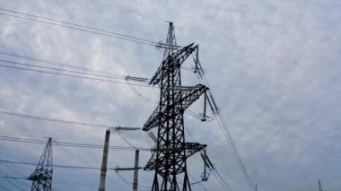 Endüstriyel boruların yanındaki elektrik direkleri. Gökyüzü arka planında yüksek voltajlı elektrik hatları var. Üretimden çıkan duman havayı kirletiyor..