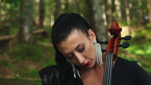 森林里有大提琴的女人一个黑发女子在绿色自然背景下演奏乐器的肖像 后续行动 — 图库视频影像