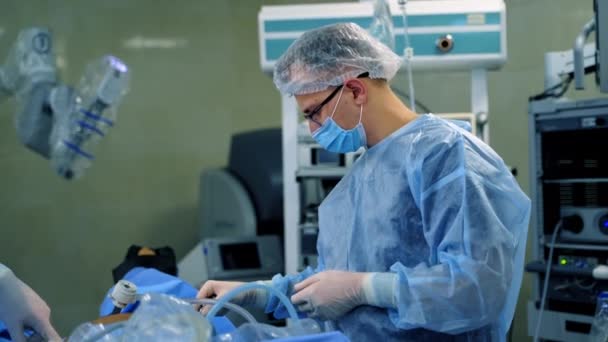 手術室の男性アシスタント ブルーメディカルユニフォームとマスクの医師は 現代の医療機器の背景で病院で手術を行います — ストック動画