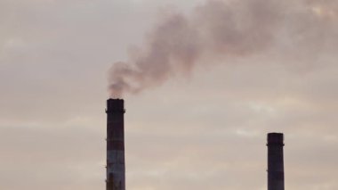 Büyük dumanlı endüstriyel borular. Zararlı emisyonlar akşam arkaplanındaki havayı dolduruyor. Yoğun dumanlar atmosferi kirletir. Ekolojik felaket. Yakın plan.
