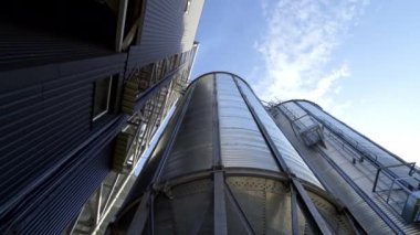 Mavi gökyüzünün altında modern tahıl ambarı. Tahıl depolamak için büyük alüminyum kaplar. Tahıl asansörlerinin dışı. Yakın plan. Aşağıdan görüntüle.