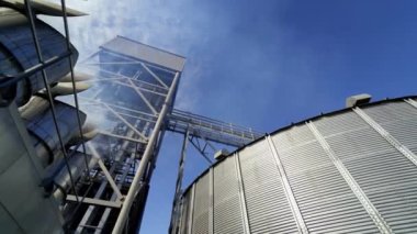 Modern tarım asansörü kompleksi. Mavi gökyüzüne karşı metal ambar. Tahıl işleme için endüstriyel ekipmanlardan yayılan duman. Aşağıdan görüntüle.