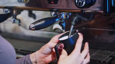 Otomatik makine kapuçino hazırlar. Kadın fincanı kahve makinesinin yanında tutuyor. Sıcak süt kadının elinde bardağa dökülüyor. Yakın plan..